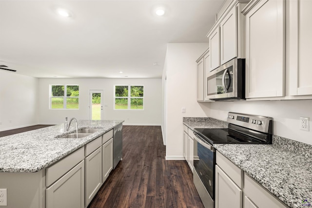 kitchen featuring light stone countertops, appliances with stainless steel finishes, dark hardwood / wood-style flooring, sink, and a center island with sink