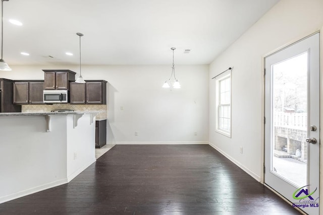 kitchen featuring hanging light fixtures, dark hardwood / wood-style flooring, backsplash, a breakfast bar area, and dark brown cabinets