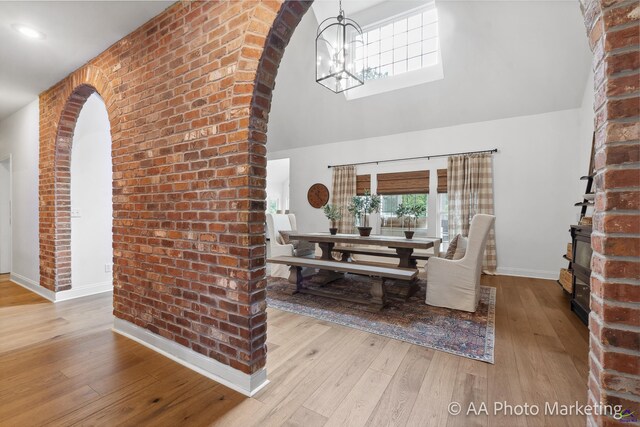 living room featuring vaulted ceiling, light hardwood / wood-style floors, brick wall, and a notable chandelier