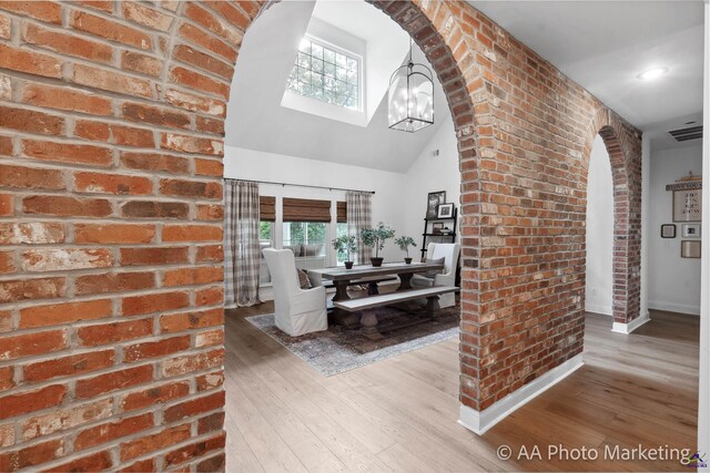 interior space with high vaulted ceiling, wood-type flooring, brick wall, and a notable chandelier