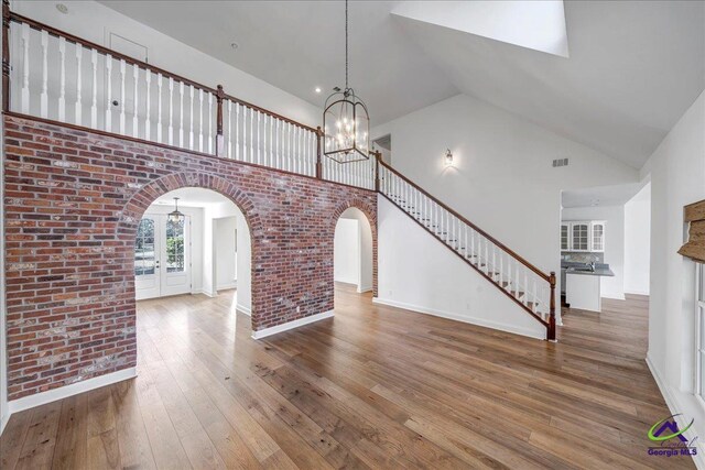 unfurnished living room with french doors, brick wall, hardwood / wood-style flooring, high vaulted ceiling, and an inviting chandelier