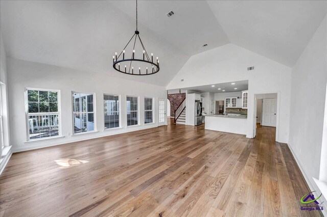 unfurnished living room with hardwood / wood-style floors, high vaulted ceiling, and an inviting chandelier