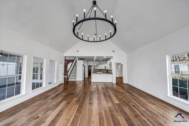 unfurnished living room featuring high vaulted ceiling, dark wood-type flooring, and an inviting chandelier