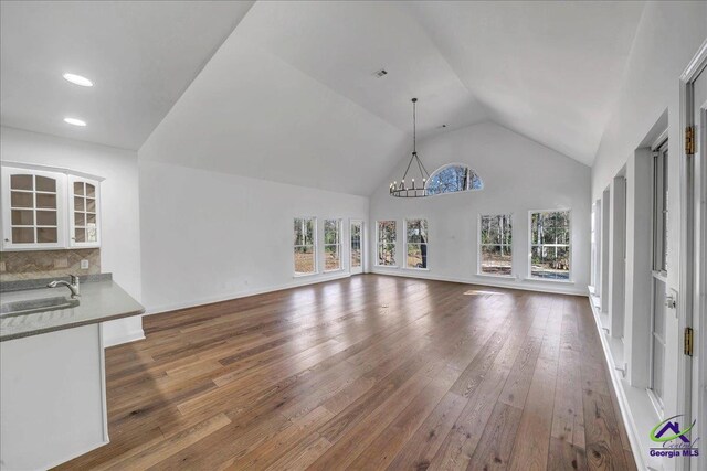 unfurnished living room featuring a notable chandelier, dark hardwood / wood-style floors, sink, and vaulted ceiling