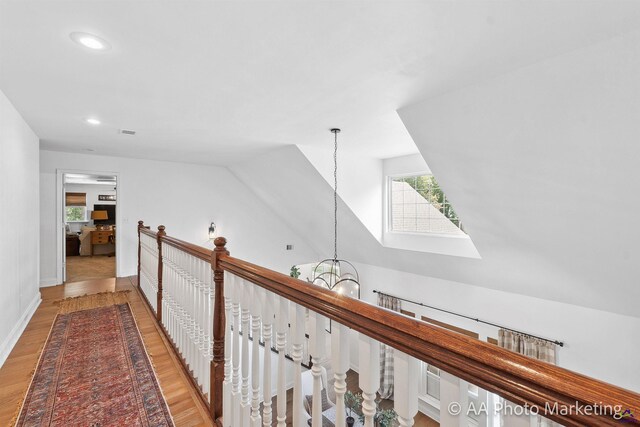 hallway with a notable chandelier, vaulted ceiling, and light wood-type flooring