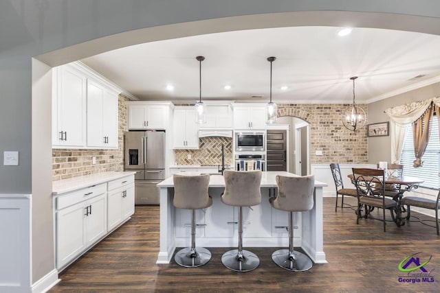 kitchen featuring white cabinets, appliances with stainless steel finishes, hanging light fixtures, and an island with sink