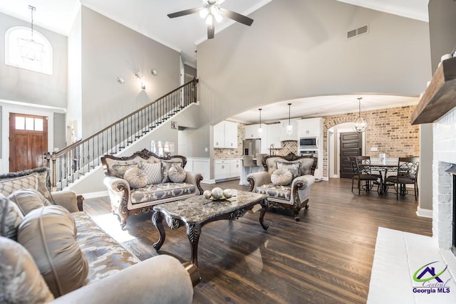 living room with ceiling fan with notable chandelier, dark hardwood / wood-style flooring, a towering ceiling, and crown molding