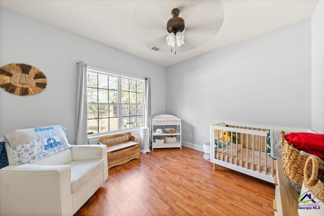 bedroom featuring ceiling fan, wood-type flooring, a textured ceiling, and a nursery area