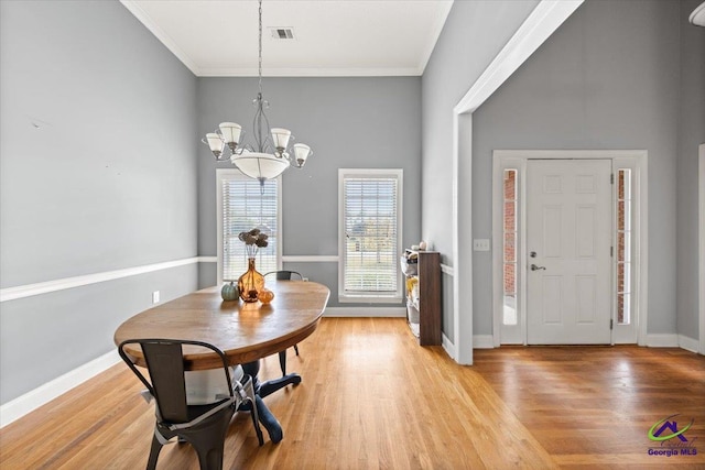 dining area featuring light hardwood / wood-style flooring, ornamental molding, a high ceiling, and a notable chandelier