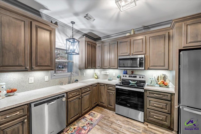 kitchen featuring appliances with stainless steel finishes, backsplash, sink, decorative light fixtures, and light hardwood / wood-style flooring