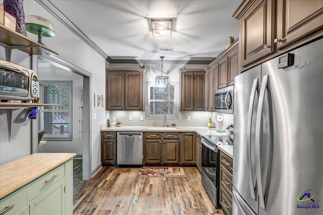 kitchen featuring sink, stainless steel appliances, wooden counters, pendant lighting, and ornamental molding