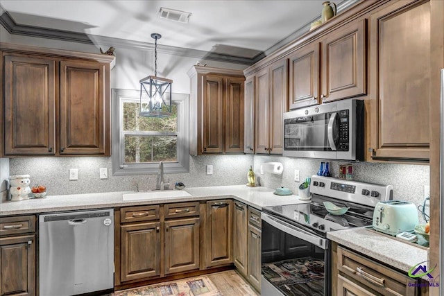 kitchen with sink, stainless steel appliances, pendant lighting, decorative backsplash, and ornamental molding