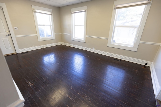 spare room featuring a paneled ceiling, a healthy amount of sunlight, and dark hardwood / wood-style flooring