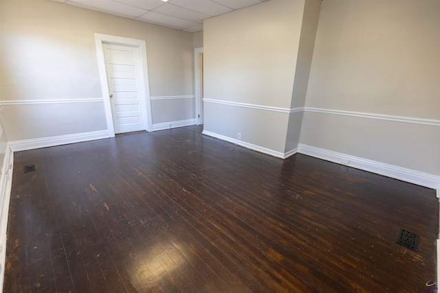 spare room with a paneled ceiling and dark hardwood / wood-style flooring