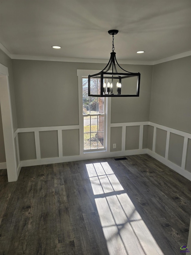 unfurnished dining area with a notable chandelier, ornamental molding, and dark wood-type flooring