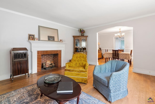 living room featuring ornamental molding, wood-type flooring, a notable chandelier, and a brick fireplace