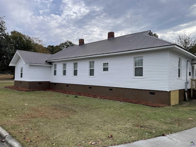 view of side of property featuring crawl space, a chimney, metal roof, and a yard