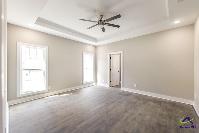 spare room with ceiling fan, a tray ceiling, and dark hardwood / wood-style flooring