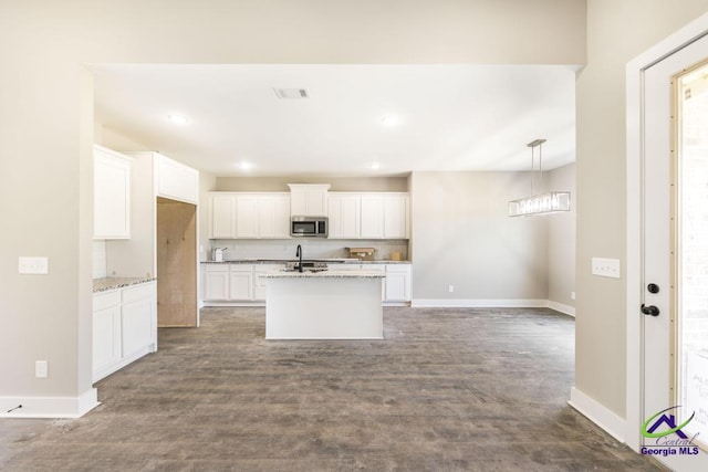 kitchen with light stone counters, an island with sink, white cabinets, dark hardwood / wood-style flooring, and decorative light fixtures