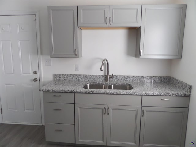 kitchen with gray cabinets, light stone counters, and sink