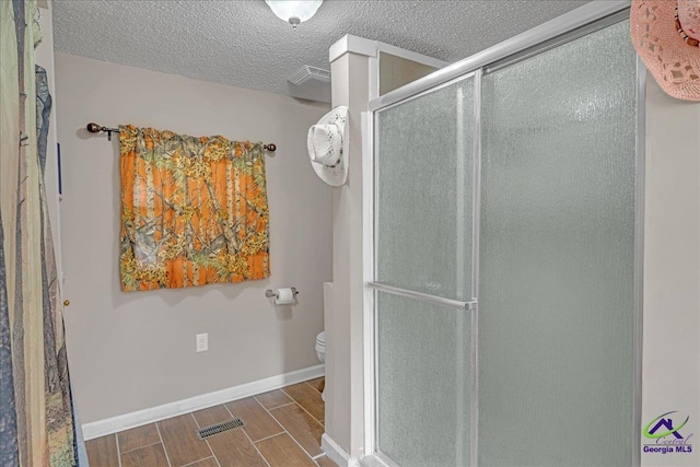 bathroom featuring toilet, a shower with shower door, and a textured ceiling