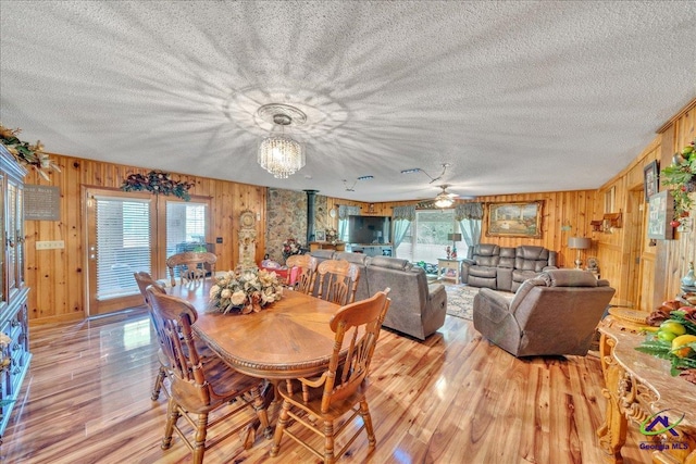 dining room featuring ceiling fan with notable chandelier, light wood-type flooring, and wooden walls