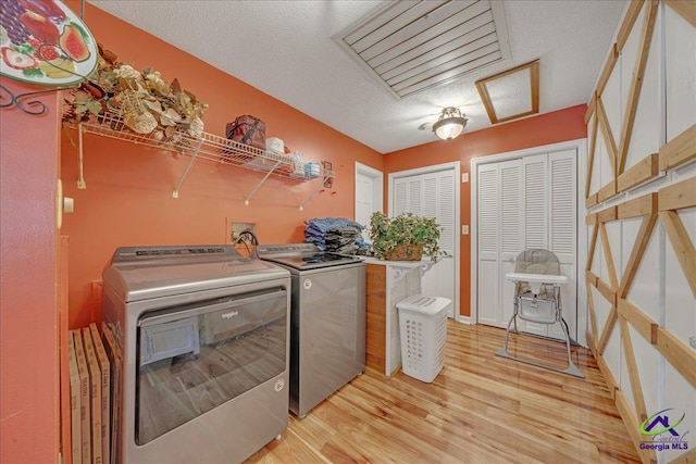 clothes washing area featuring washer and clothes dryer, light wood-type flooring, and a textured ceiling