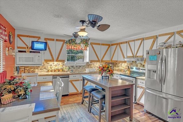 kitchen featuring appliances with stainless steel finishes, light wood-type flooring, ceiling fan, sink, and white cabinets