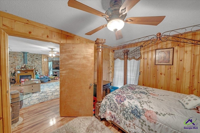 bedroom featuring a textured ceiling, light wood-type flooring, ceiling fan, and wooden walls