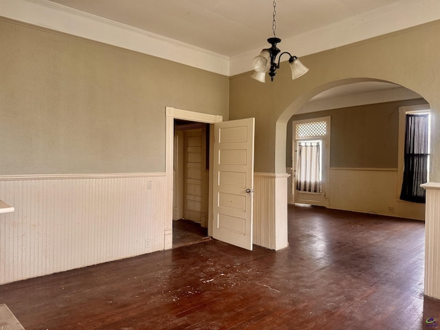 empty room with dark hardwood / wood-style floors, crown molding, and a chandelier