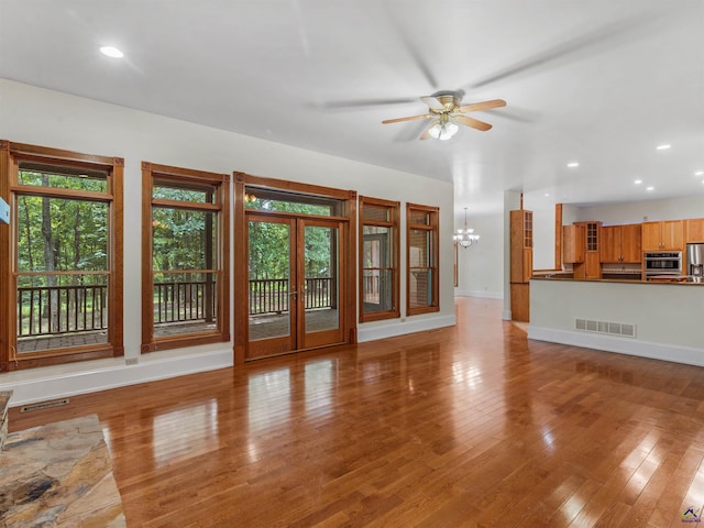 unfurnished living room featuring ceiling fan with notable chandelier, a healthy amount of sunlight, light hardwood / wood-style floors, and french doors