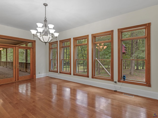 unfurnished dining area with hardwood / wood-style floors, french doors, and a chandelier