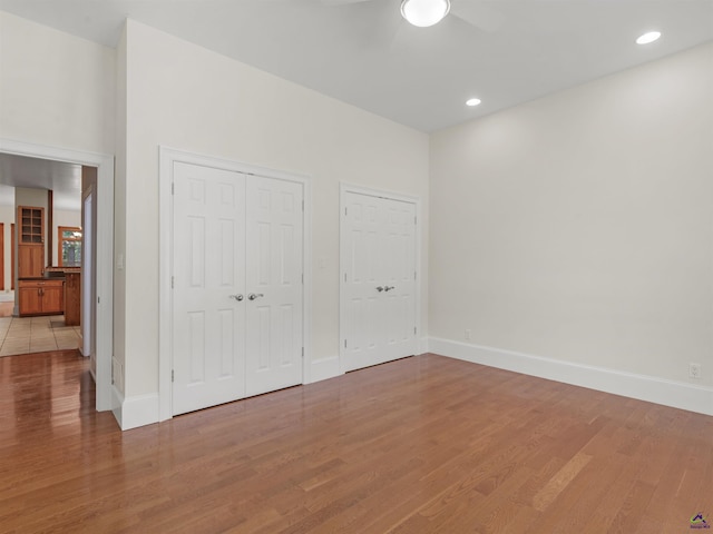 unfurnished bedroom with ceiling fan, light hardwood / wood-style floors, and two closets