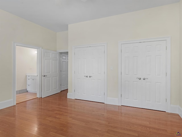 unfurnished bedroom featuring ensuite bathroom, light wood-type flooring, and two closets