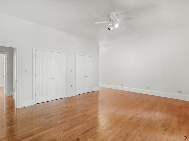 unfurnished bedroom featuring light hardwood / wood-style flooring, ceiling fan, and multiple closets