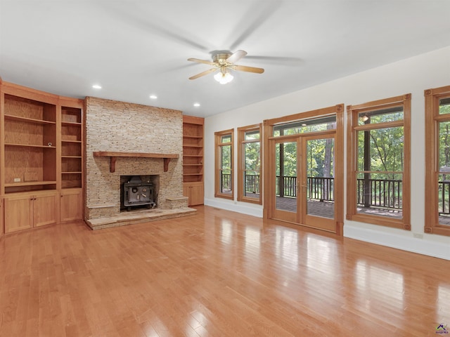 unfurnished living room with a wood stove, french doors, built in features, and ceiling fan