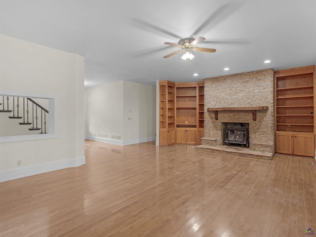 unfurnished living room featuring built in shelves, hardwood / wood-style flooring, a wood stove, and ceiling fan