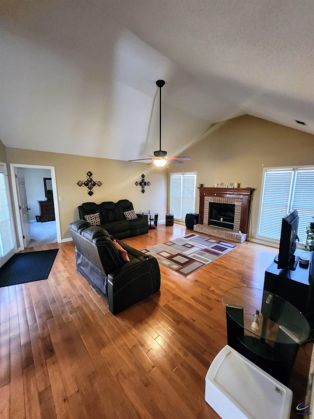 living room featuring a textured ceiling, ceiling fan, a fireplace, hardwood / wood-style floors, and lofted ceiling