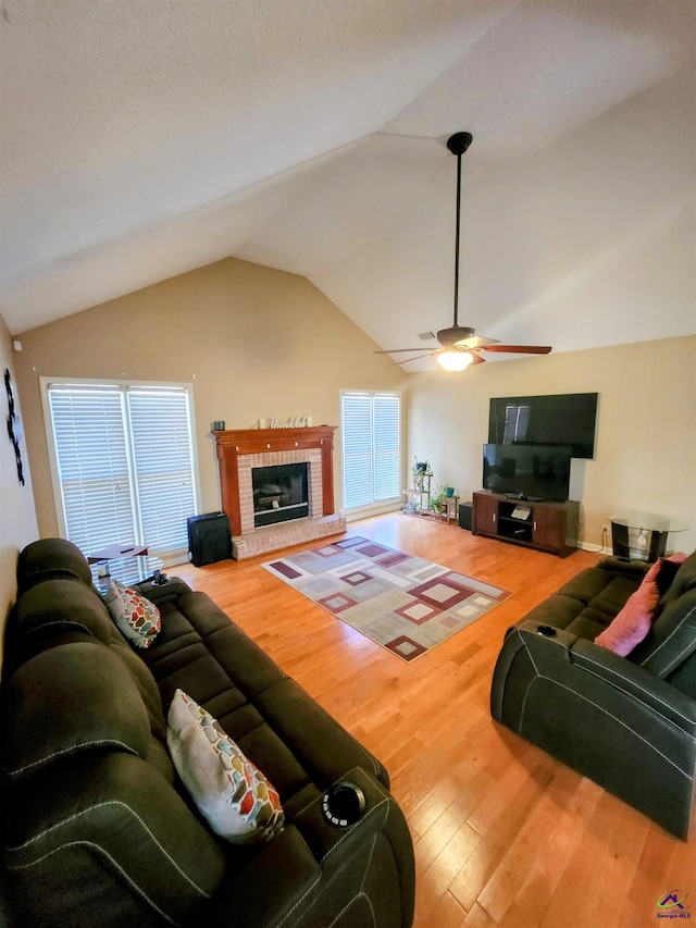 living room featuring ceiling fan, wood-type flooring, lofted ceiling, and a brick fireplace