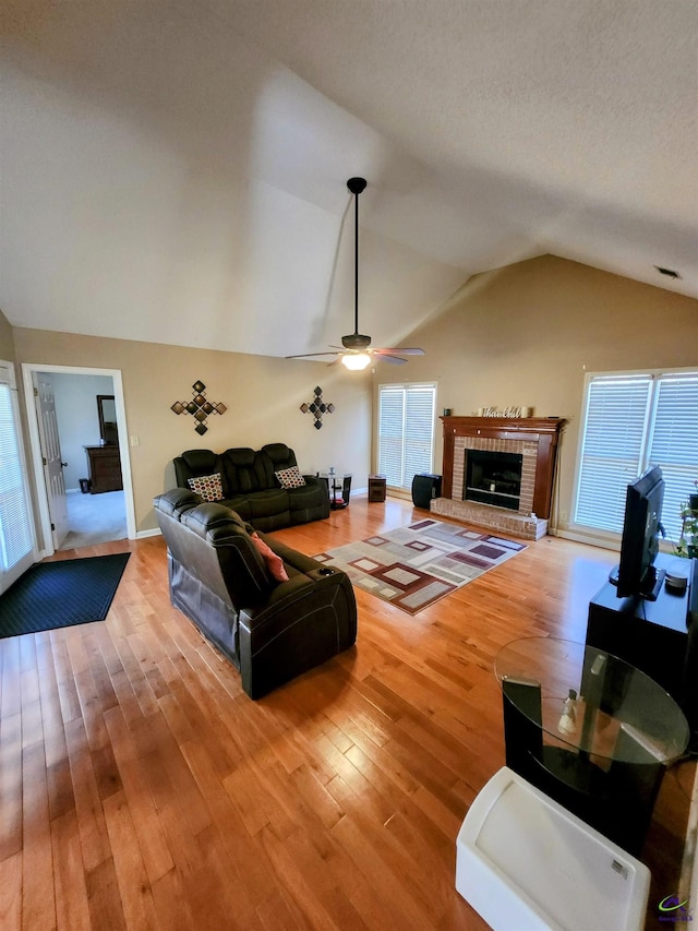 living room featuring ceiling fan, a fireplace, light hardwood / wood-style floors, and lofted ceiling