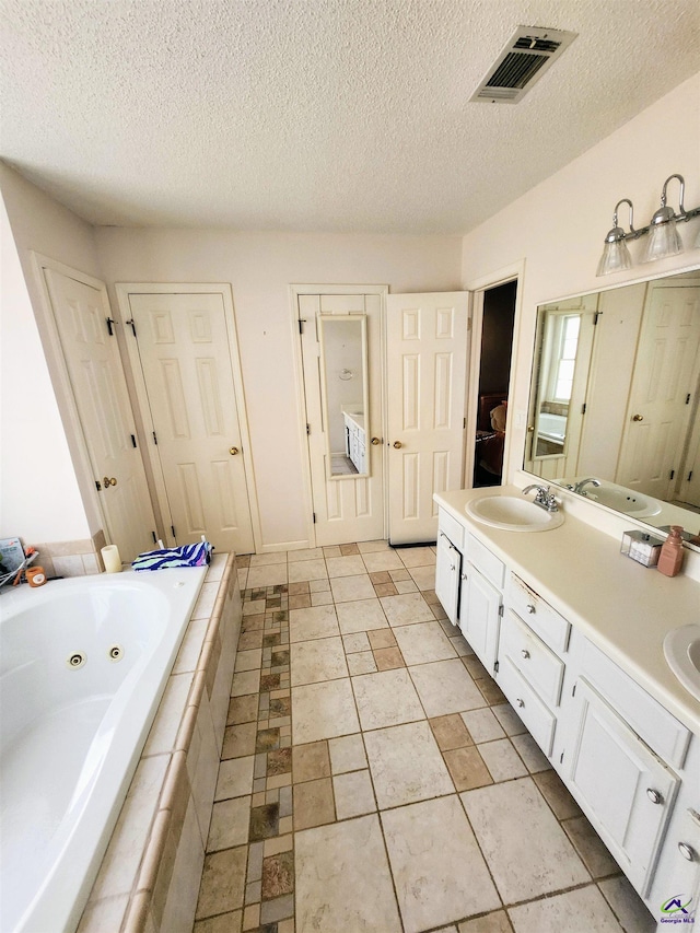 bathroom with vanity, a relaxing tiled tub, and a textured ceiling