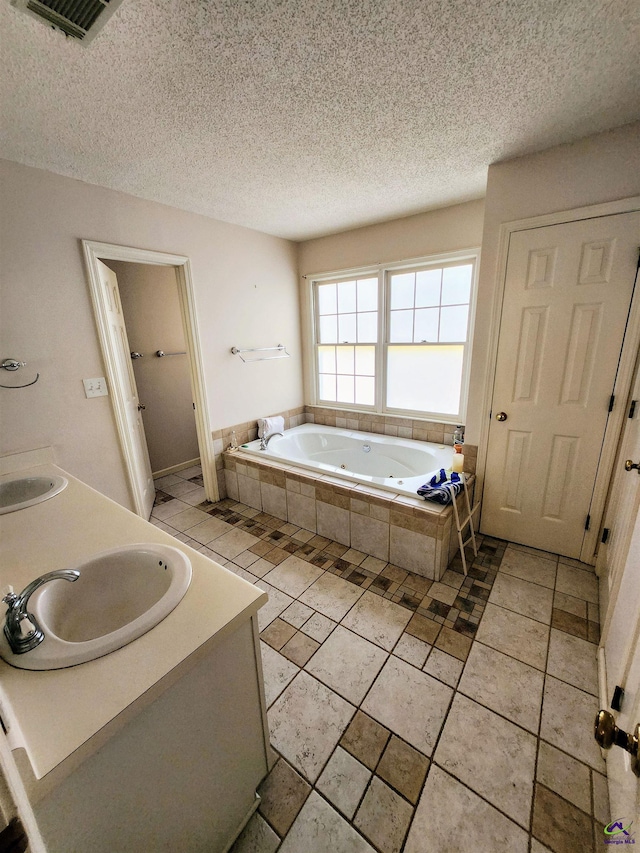 bathroom featuring vanity, a relaxing tiled tub, and a textured ceiling