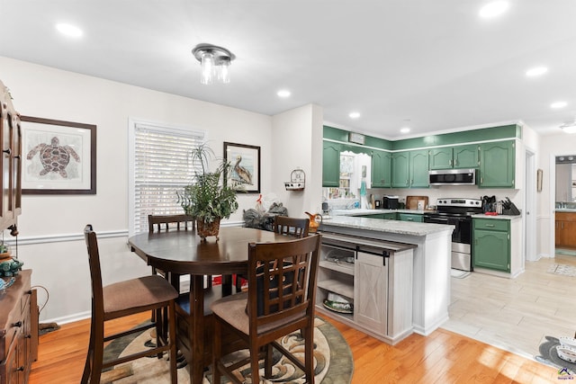 kitchen with green cabinets, kitchen peninsula, appliances with stainless steel finishes, and light hardwood / wood-style flooring