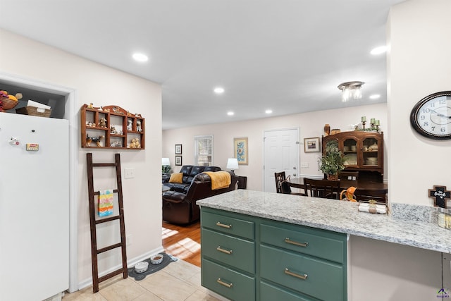 kitchen featuring light stone countertops, white fridge, and green cabinetry