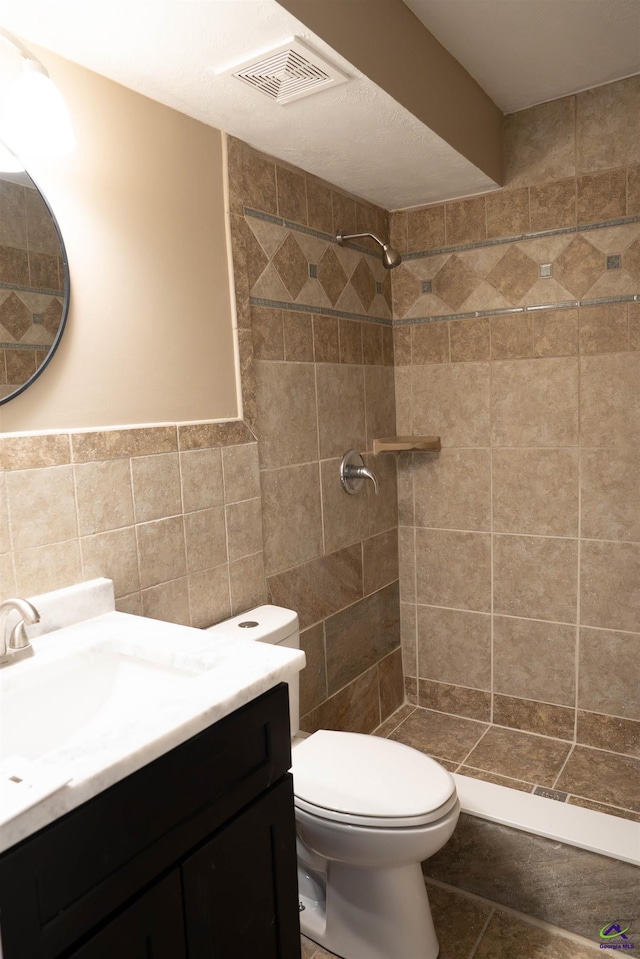 bathroom featuring toilet, a tile shower, tile walls, and vanity