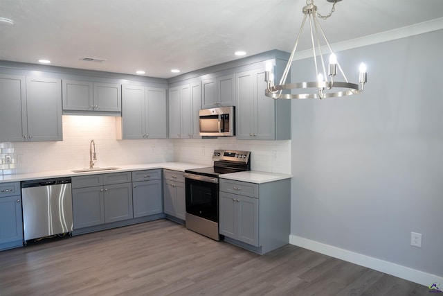 kitchen with gray cabinets, appliances with stainless steel finishes, light wood-type flooring, hanging light fixtures, and sink