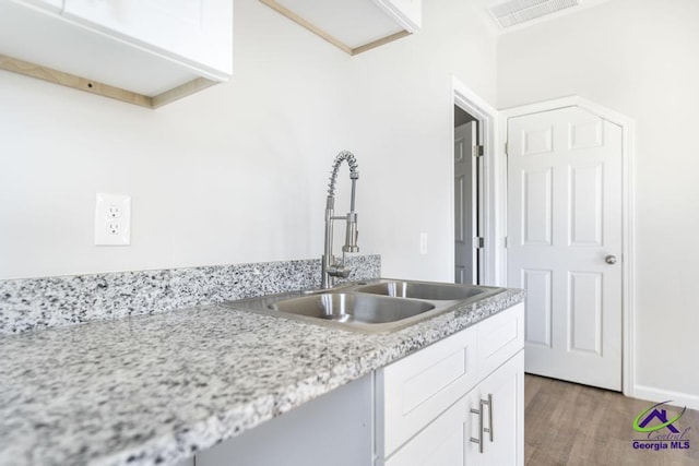 kitchen with wood-type flooring, white cabinets, light stone counters, and sink