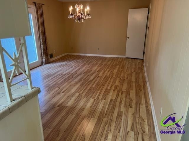 spare room with light hardwood / wood-style floors and a notable chandelier