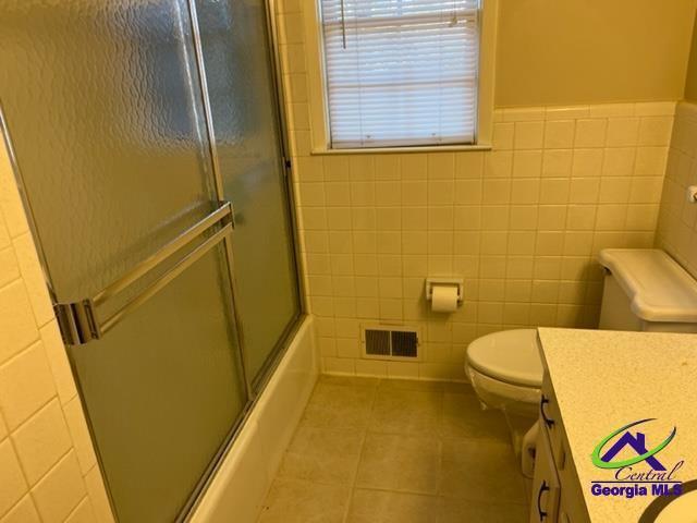 full bathroom featuring vanity, tile patterned floors, bath / shower combo with glass door, toilet, and tile walls