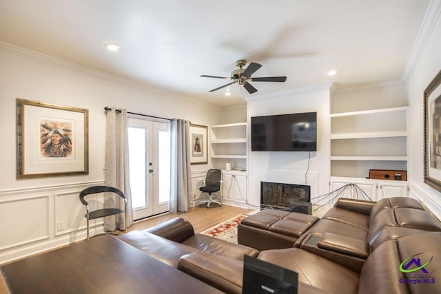 living room with french doors, crown molding, built in shelves, ceiling fan, and light hardwood / wood-style floors